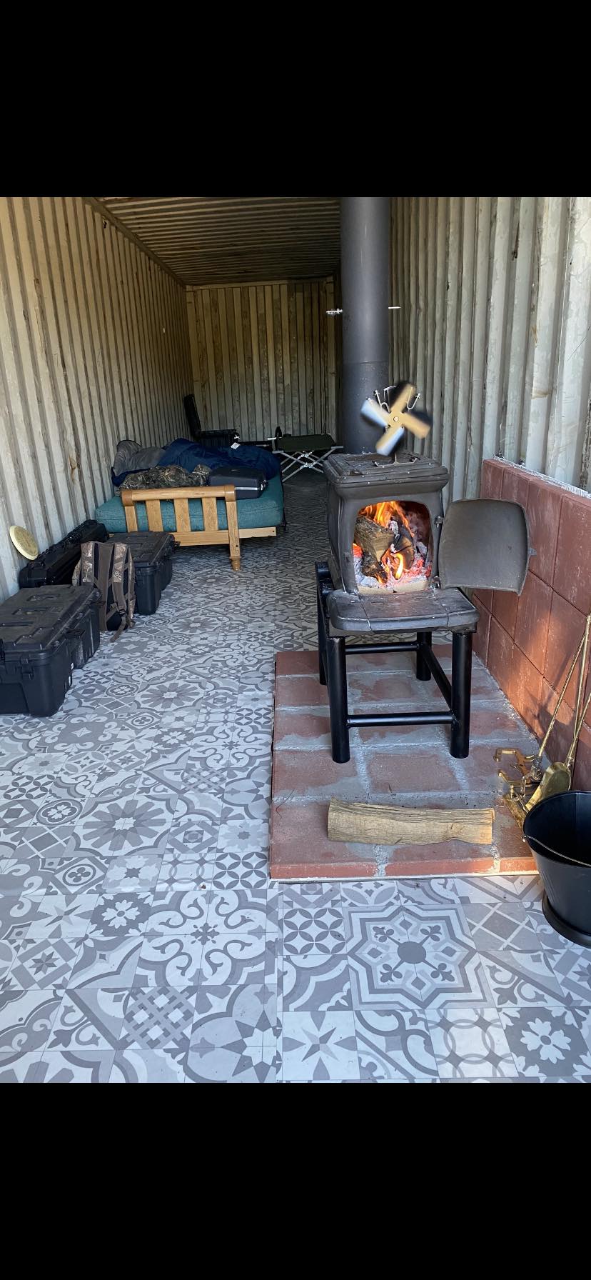 The meme is a split-screen image showing two different environments. On the left, a cozy cabin with a fireplace and a comfortable chair, with a sign that reads "Welcome to the Cabin". On the right, a cramped and dirty shipping container with a sign that reads "Welcome to the Shipping Container". The text at the top of the image reads "When you're trying to be cozy but your roommate is a shipping container".